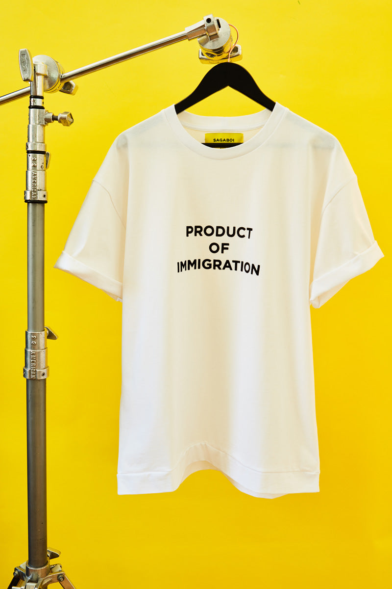 Image of Sagaboi's Product Of Immigration Slogan T-shirt Hung On a C Stand